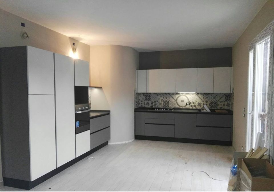 Cucina moderna con mobili bianchi e grigi, ripiani scuri e paraschizzi fantasia.