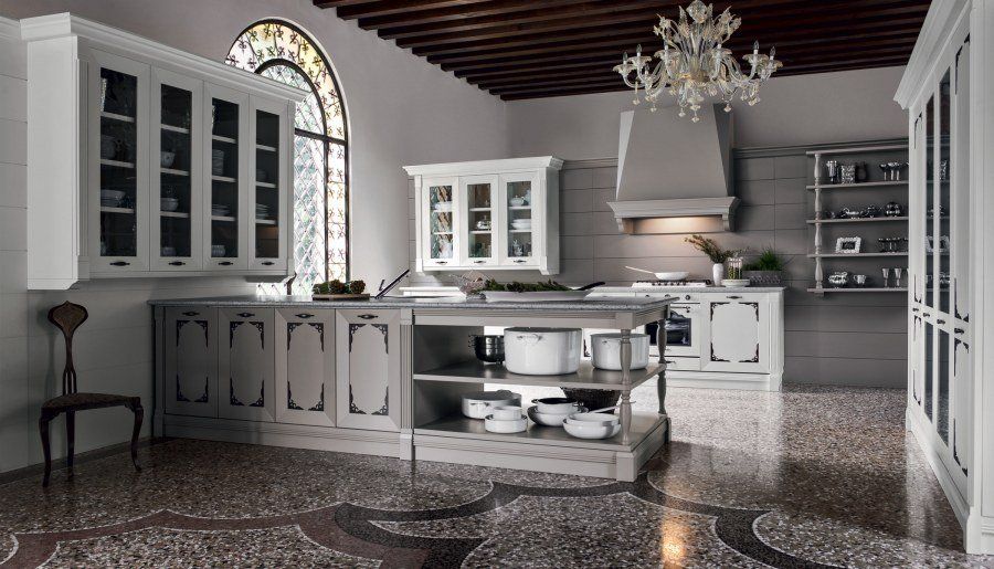 Elegante cucina grigia e bianca con isola, mobili, lampadario e pavimento decorativo.