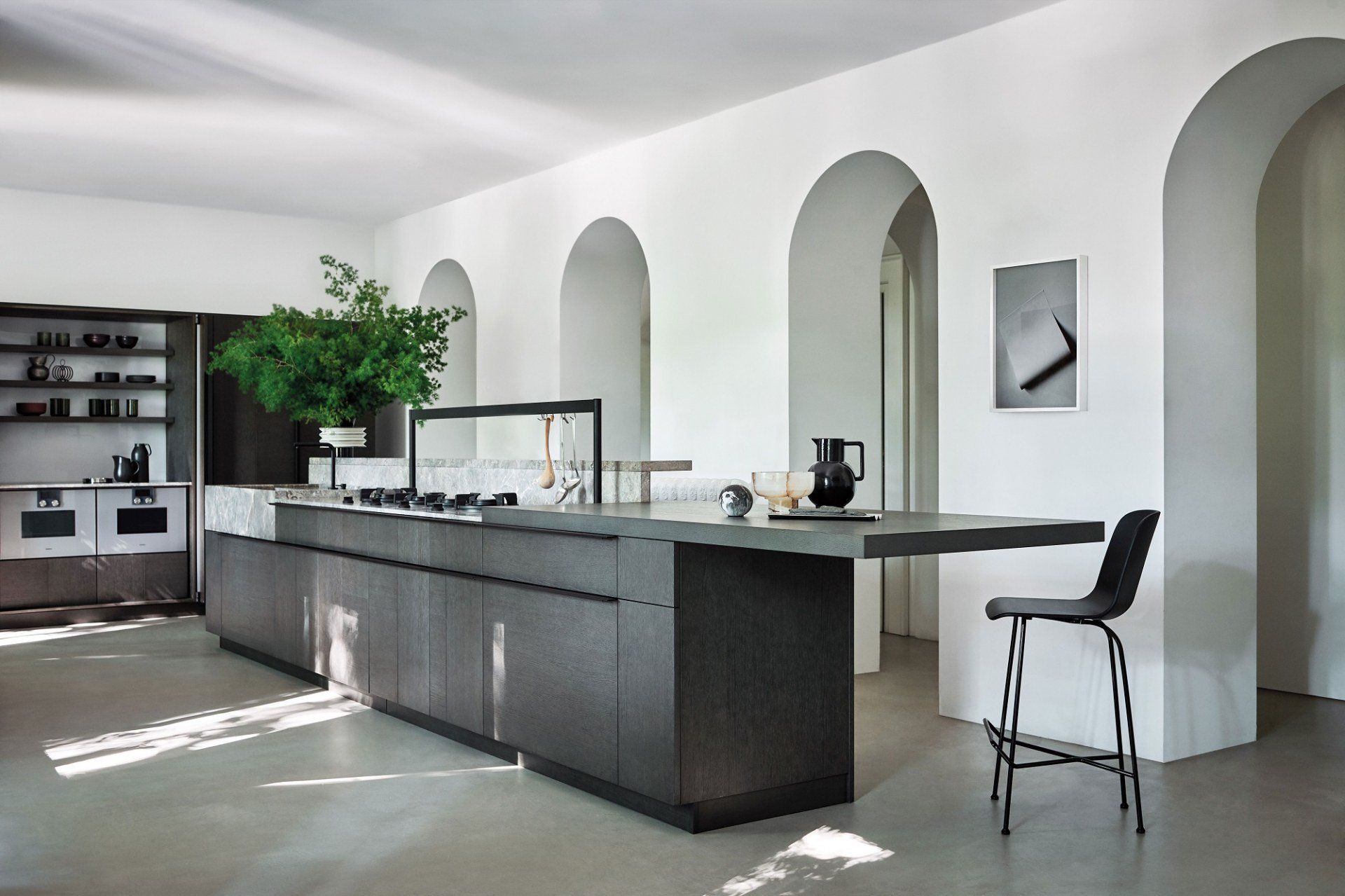 Cucina moderna con isola grigia, alti archi bianchi e una semplice sedia nera.