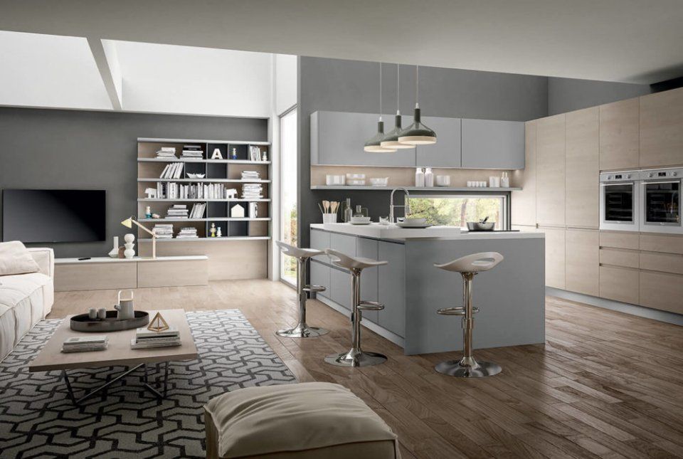 Moderna cucina open space e soggiorno con mobili grigi e beige, isola con sgabelli e pavimenti in legno.
