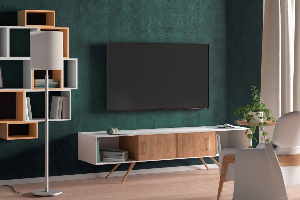 Soggiorno con parete color verde acqua scuro, TV, mobile porta TV bianco e legno, libreria e lampada.