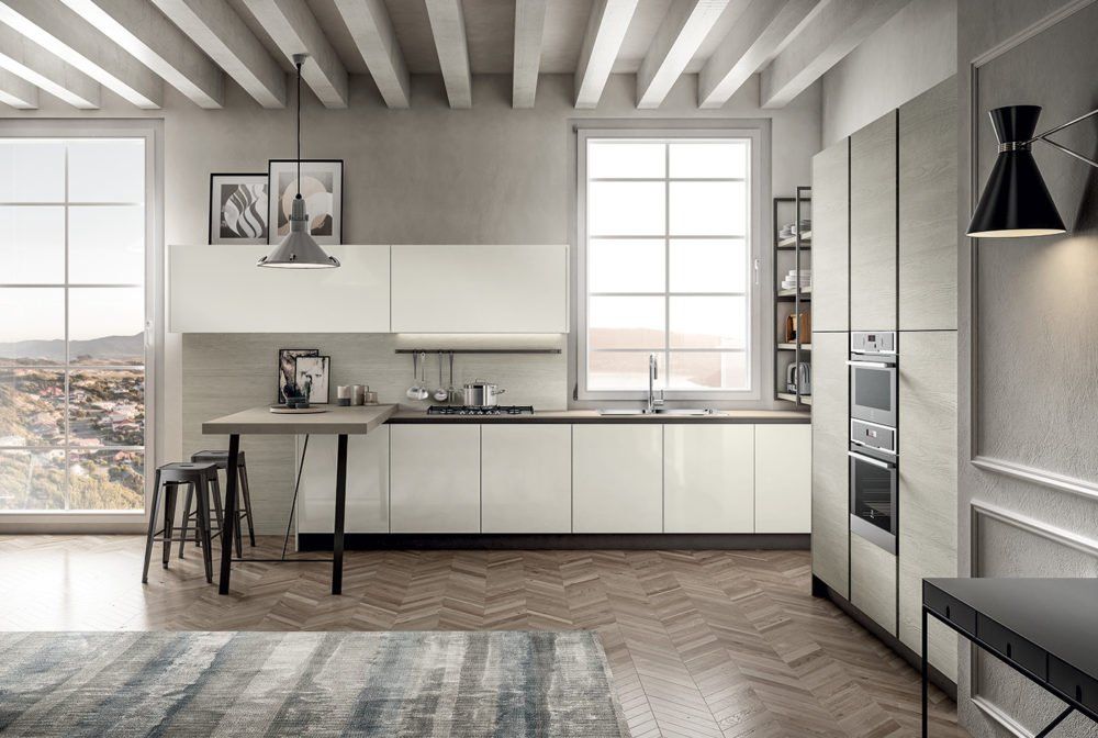 Cucina moderna con mobili chiari, pavimento in legno, ampie finestre e una piccola zona pranzo.