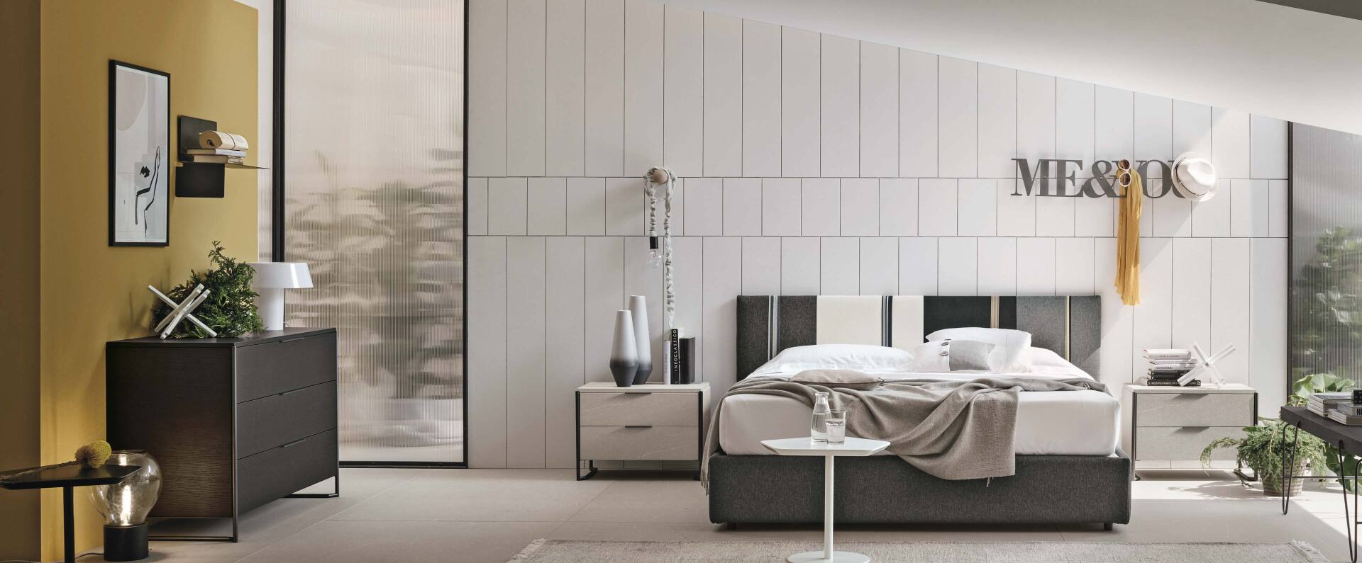 Camera da letto moderna con mobili bianchi e grigi, ampia finestra, opere d'arte e dettagli decorativi.