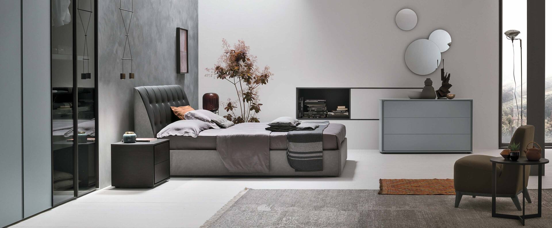 Camera da letto con letto, comodino, cassettiera e poltrona. Combinazione di colori grigio e bianco.
