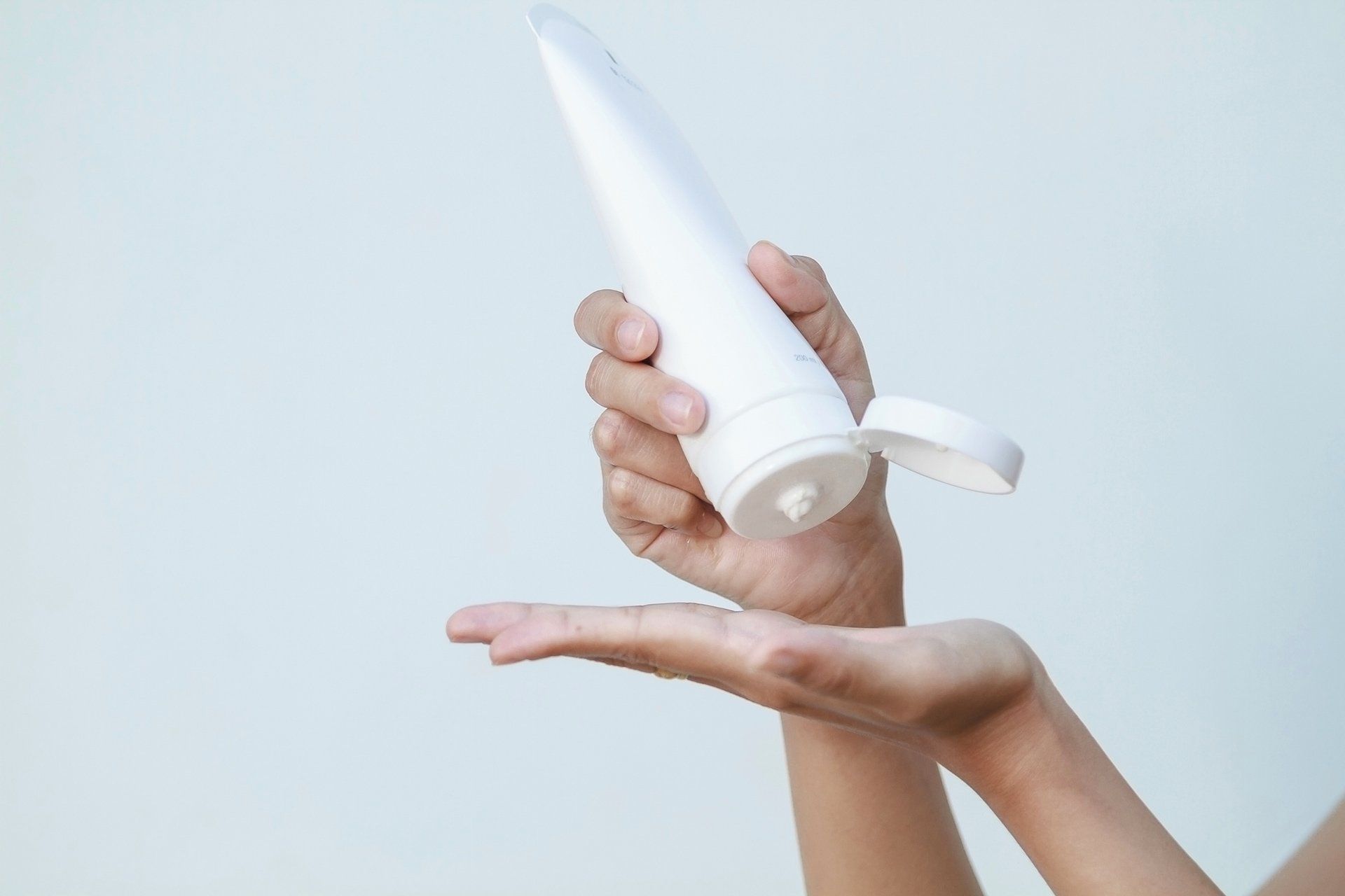 Eine Frau hält eine weiße Tube Lotion in der Hand.