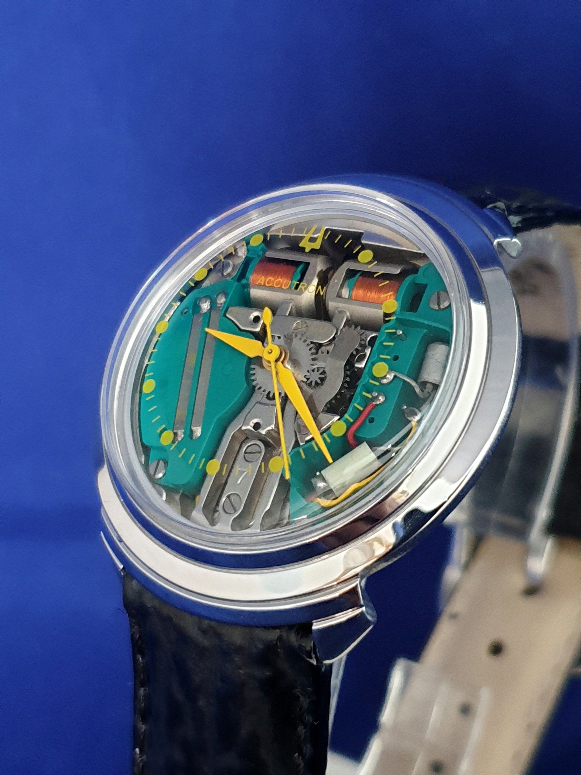 Transparent skeleton wristwatch with yellow hands on a blue background