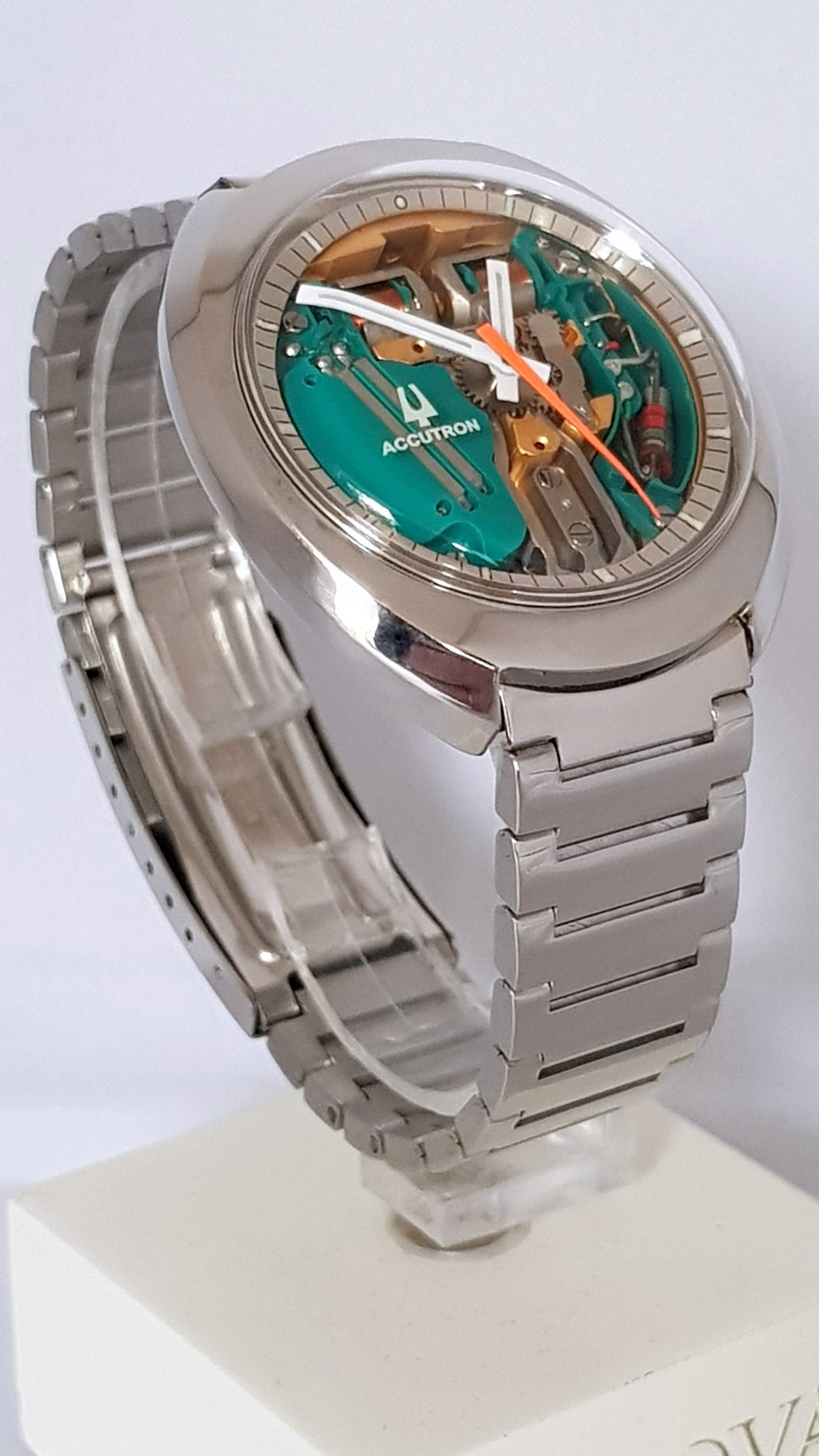 Silver wristwatch with green dial and orange accents on a display stand