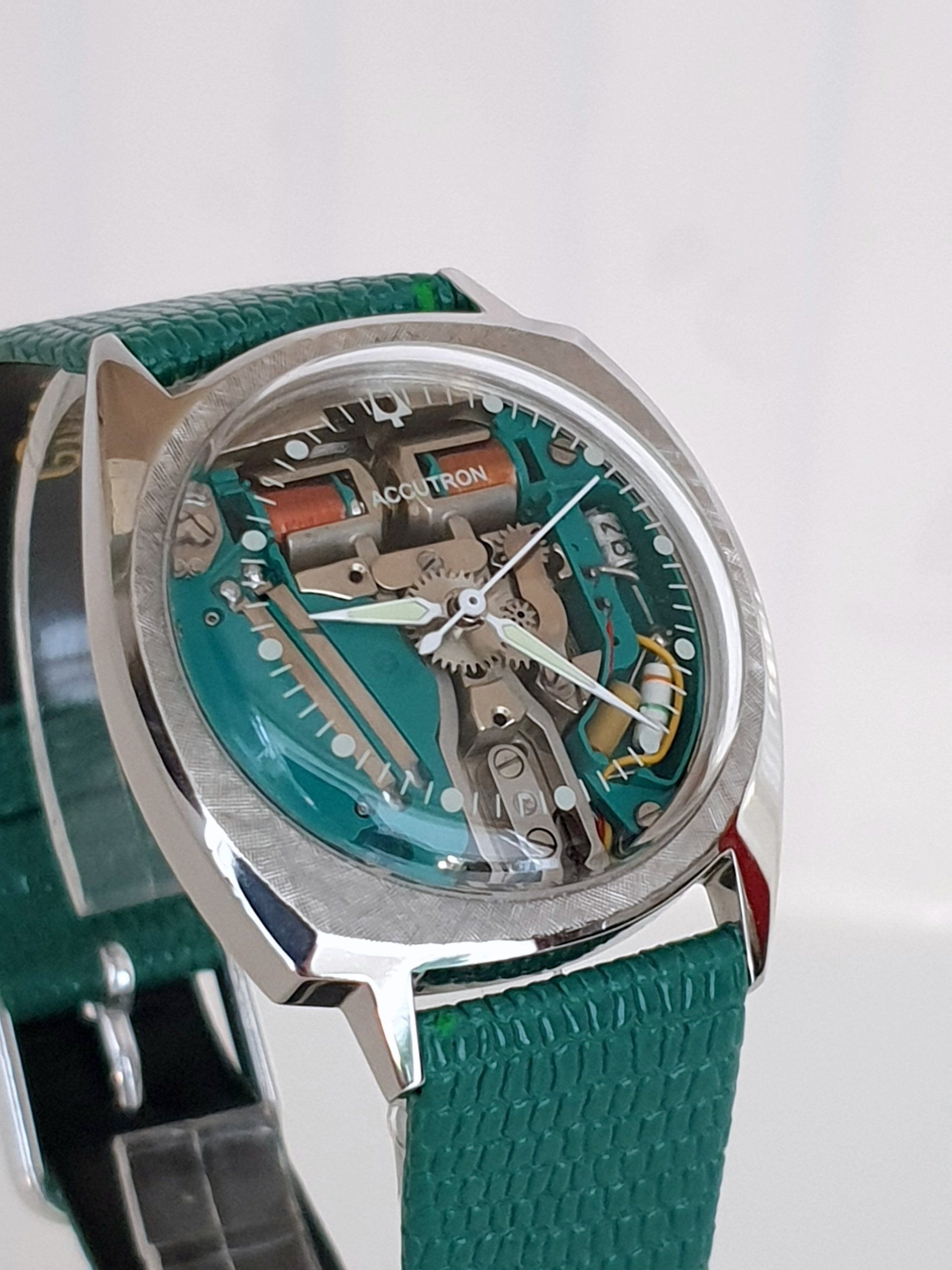 Close-up of a transparent skeleton wristwatch with a teal dial and green strap
