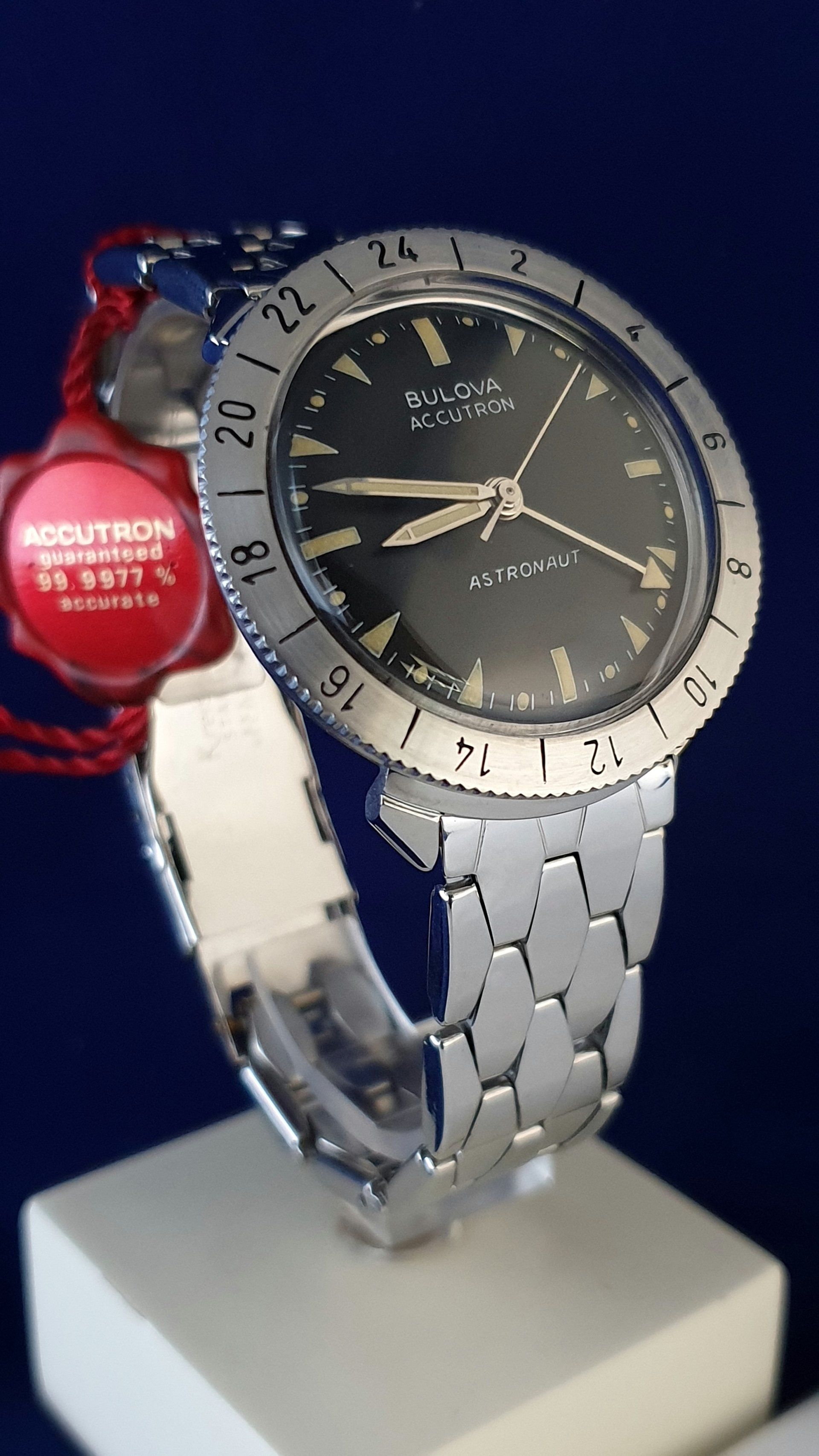 Silver wristwatch with a dark face on a white stand, next to a red price tag.