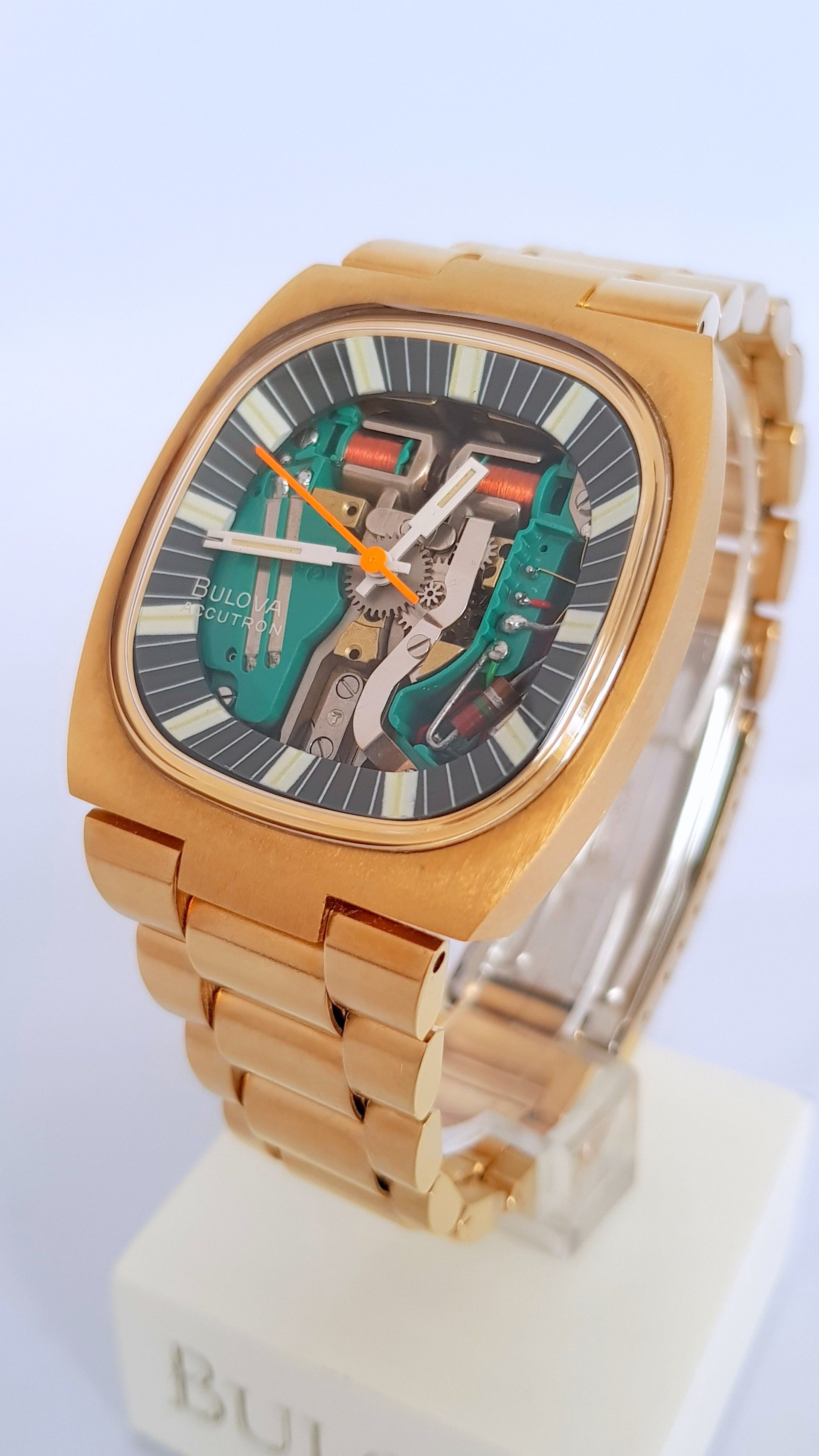 Gold-toned wristwatch with a square face and colorful dial on a display stand