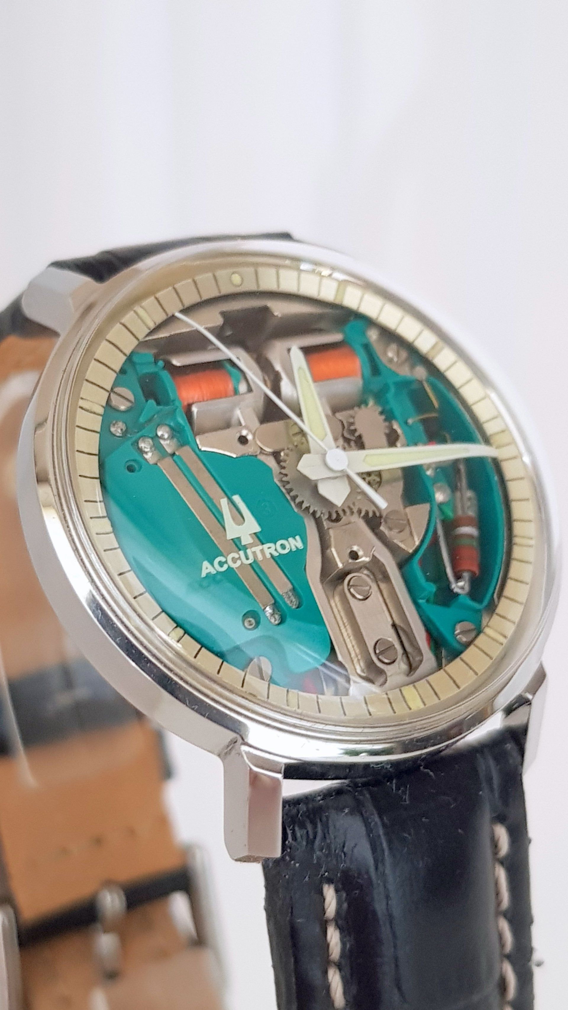 Close-up of a teal skeleton wristwatch with a black leather strap and silver case