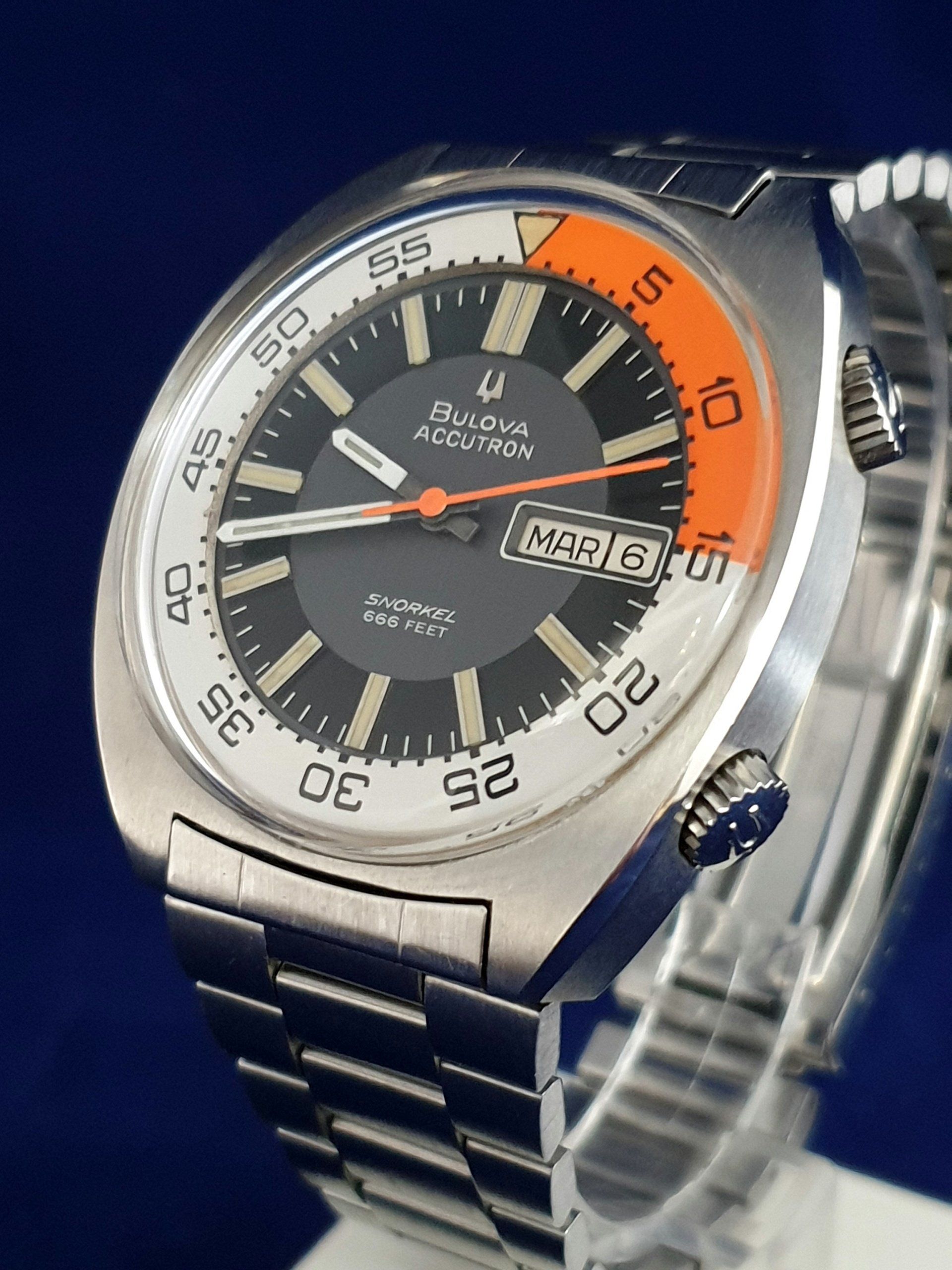 Silver Bulova wristwatch with orange accents and day-date display on a metal band