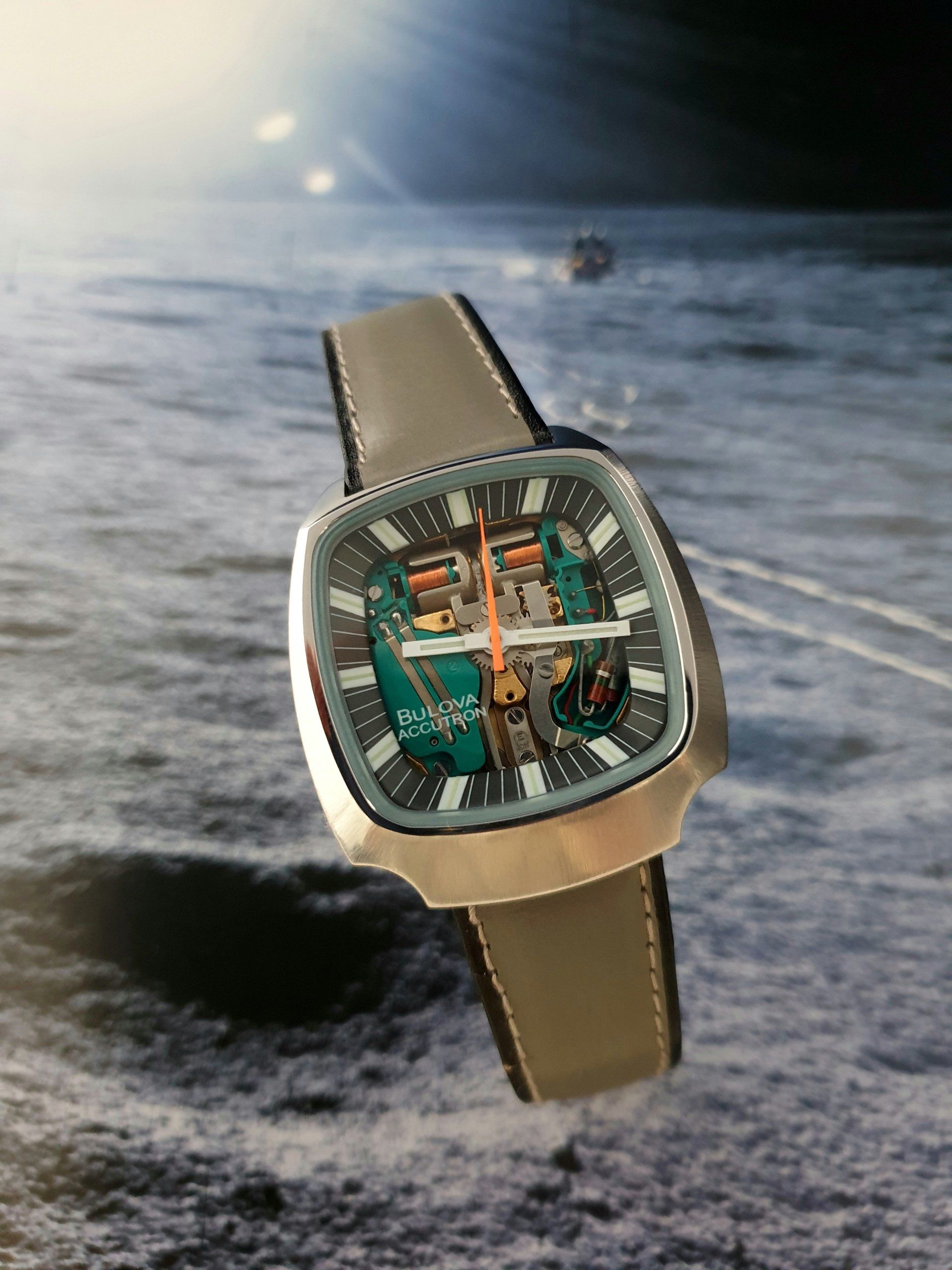 Luxury square wristwatch with beige strap over a moonlike landscape background