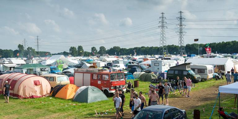 Een drukke camping met tenten, caravans en voertuigen. Mensen lopen op een grasveld op een zonnige dag.