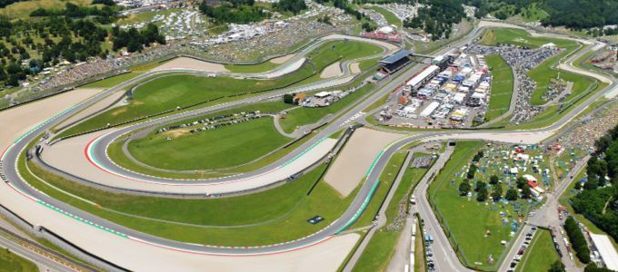 Luchtfoto van het Red Bull Ring-racecircuit. Het circuit slingert zich door groene heuvels, met zichtbare tribunes en gebouwen.