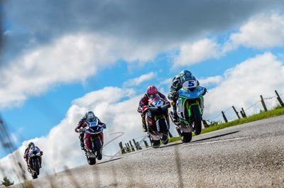 Motorrace op een bochtige weg tegen een bewolkte hemel. Verschillende coureurs leunen in de bochten en rijden met hoge snelheid.