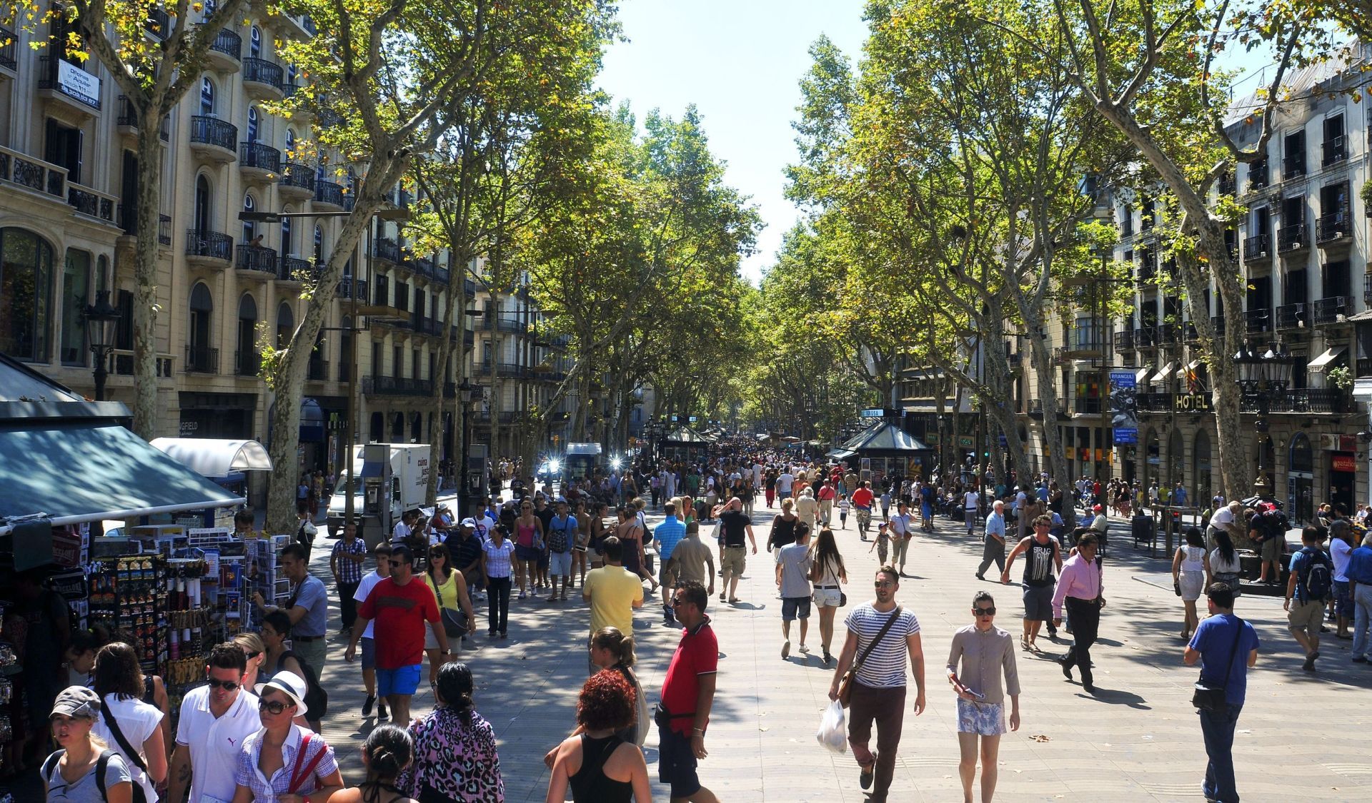 Een drukke voetgangersstraat in Barcelona, omzoomd met bomen en gebouwen, vol met wandelende mensen.