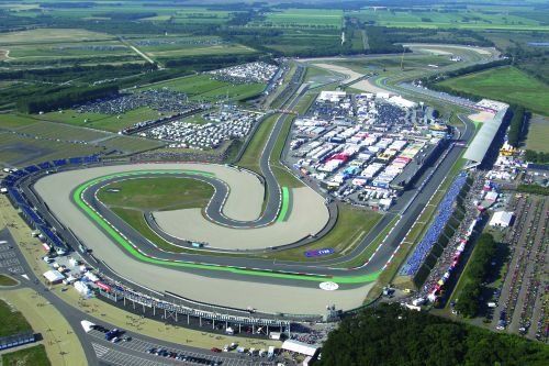 Luchtfoto van een racebaan met een groene, gebogen indeling, omgeven door paddocks, parkeerplaatsen en bomen.