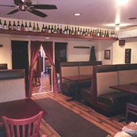 Interior of a restaurant with booths, a wine rack, wooden floor, and red curtains.