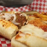 Meatball sub with melted cheese in red and white checkered basket.