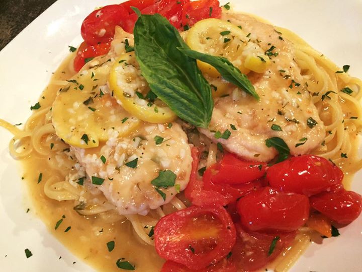 Chicken piccata with pasta, tomatoes, and lemon slices on a white plate.