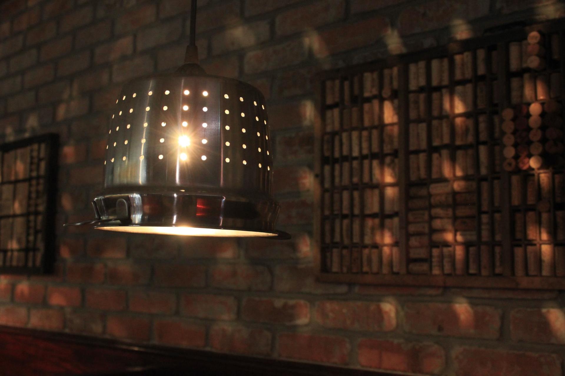A metallic, perforated lamp hanging from a brick wall casts light and shadows.