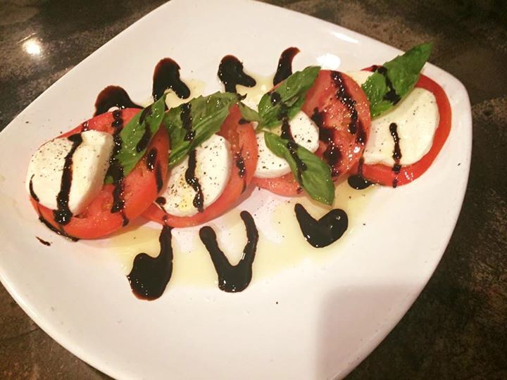 Caprese salad: tomato slices, mozzarella, basil, balsamic glaze, and olive oil on a white plate.