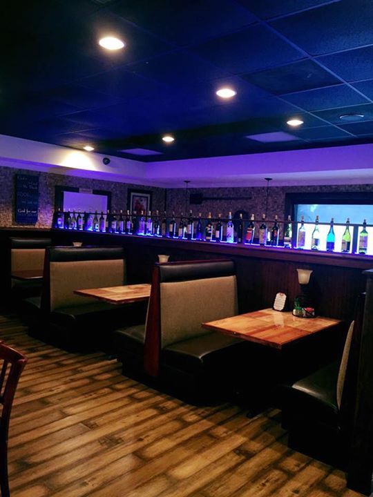 Restaurant booth seating with dim lighting, wooden floors, and a bar area with bottles.