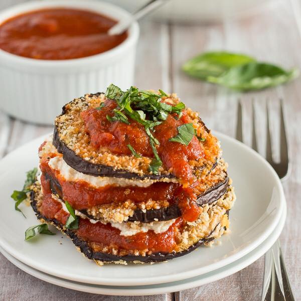 Eggplant parmesan stack on white plates with marinara sauce and basil.