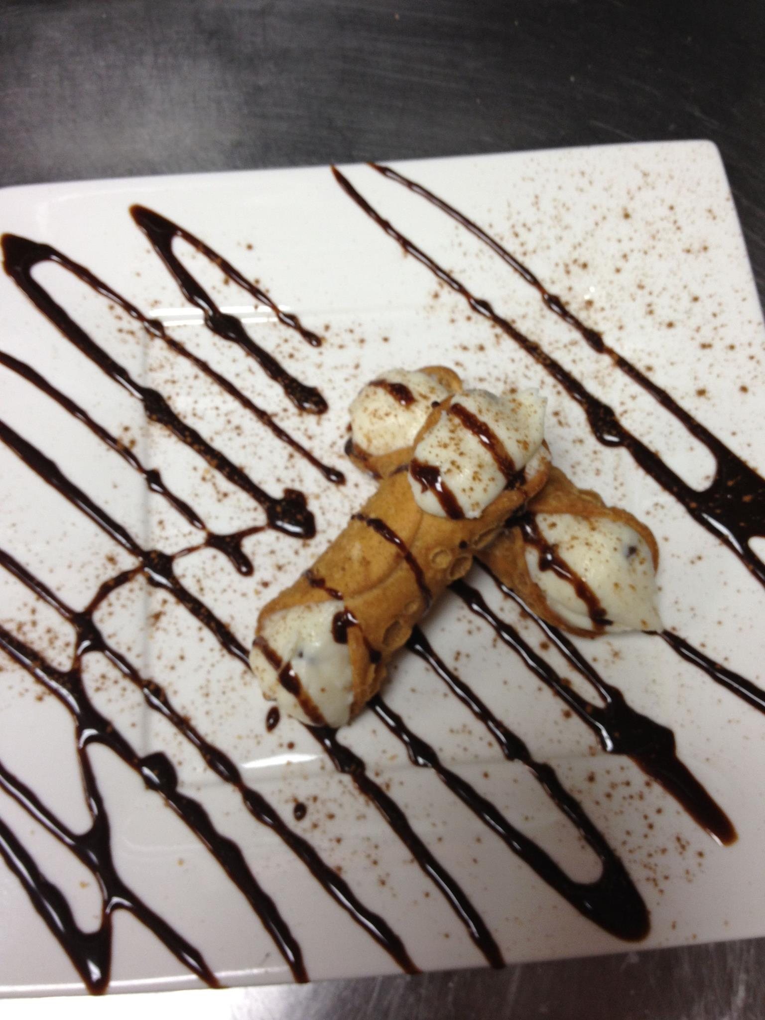 Two cannoli on a white plate, drizzled with chocolate and dusted with cocoa.