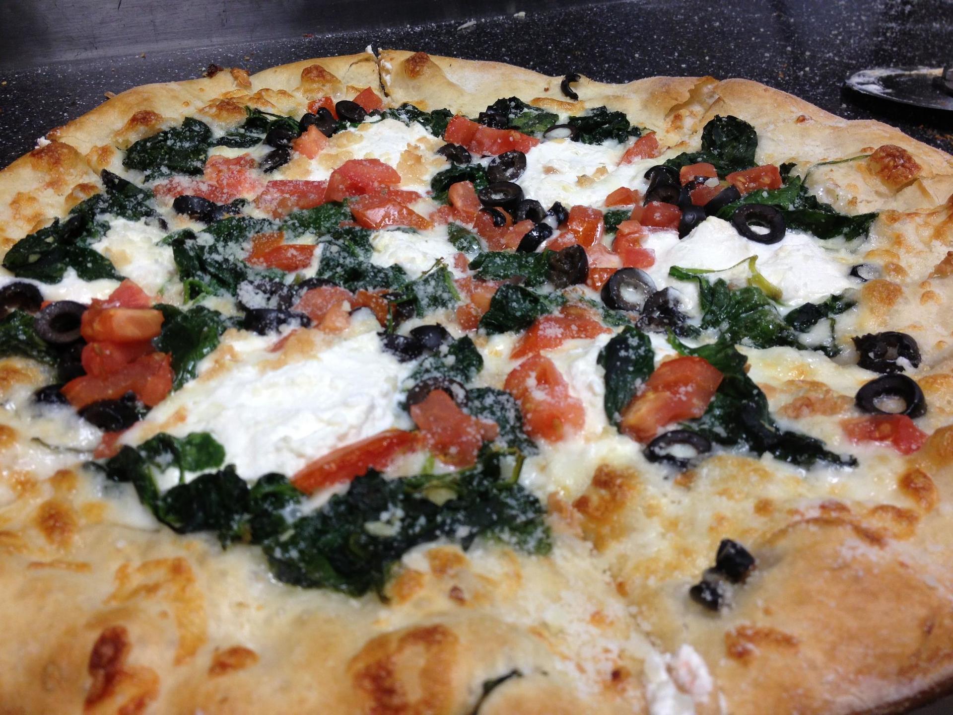 Pizza with spinach, ricotta, tomatoes, and olives on a white crust.