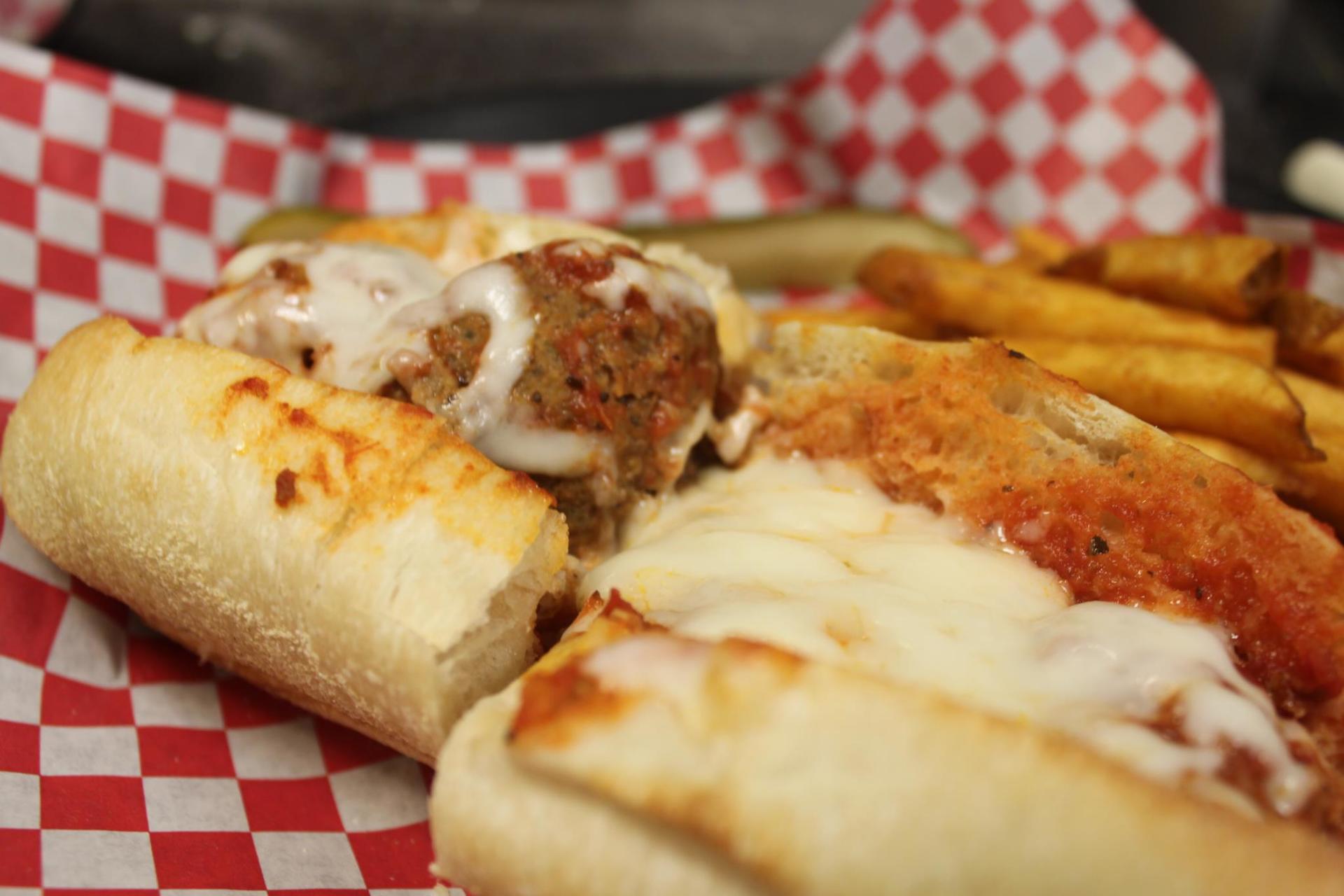Meatball sub with fries on red and white checkered paper.