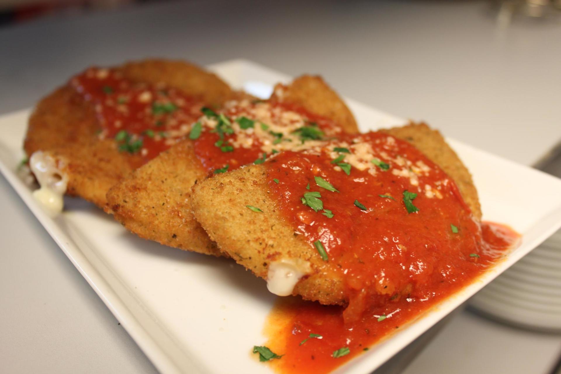 Fried mozzarella sticks with red sauce and garnish on a white plate.