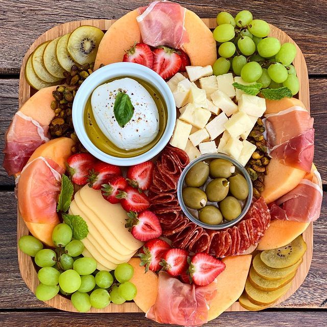 A wooden tray filled with a variety of fruits and meats