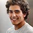 a man with curly hair is smiling and wearing a white shirt .
