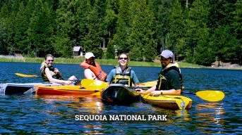 Four people in kayaks on a lake in Sequoia National Park; they wear life vests and hold paddles.