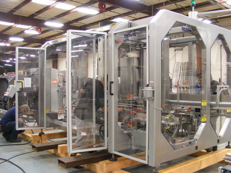 Machinery in a factory. Workers are inspecting a large, silver machine with glass panels.