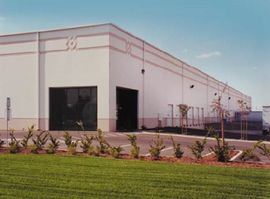 Large, light-colored industrial building with a loading dock and manicured lawn.