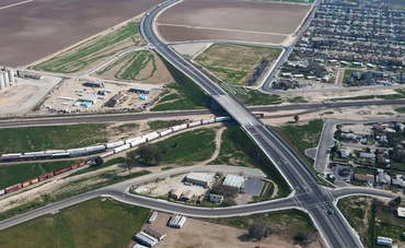 Aerial view of a highway overpass spanning a railroad track and residential area, with fields in the background.