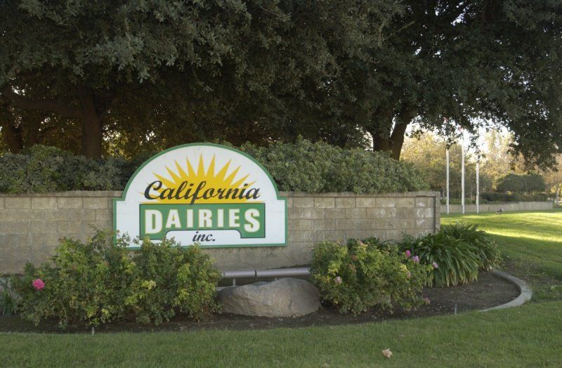 Sign for California Dairies Inc. with a sunburst design on a brick wall.