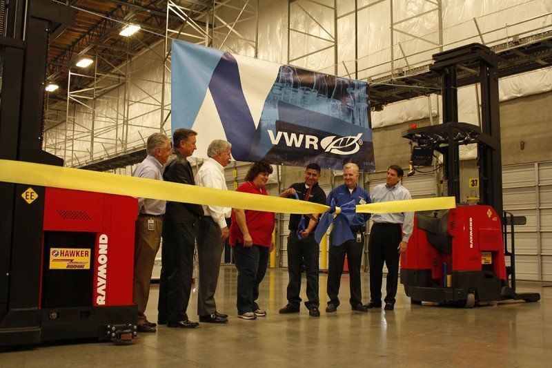 People cutting a yellow ribbon with forklifts on either side, in front of a banner for VWR.