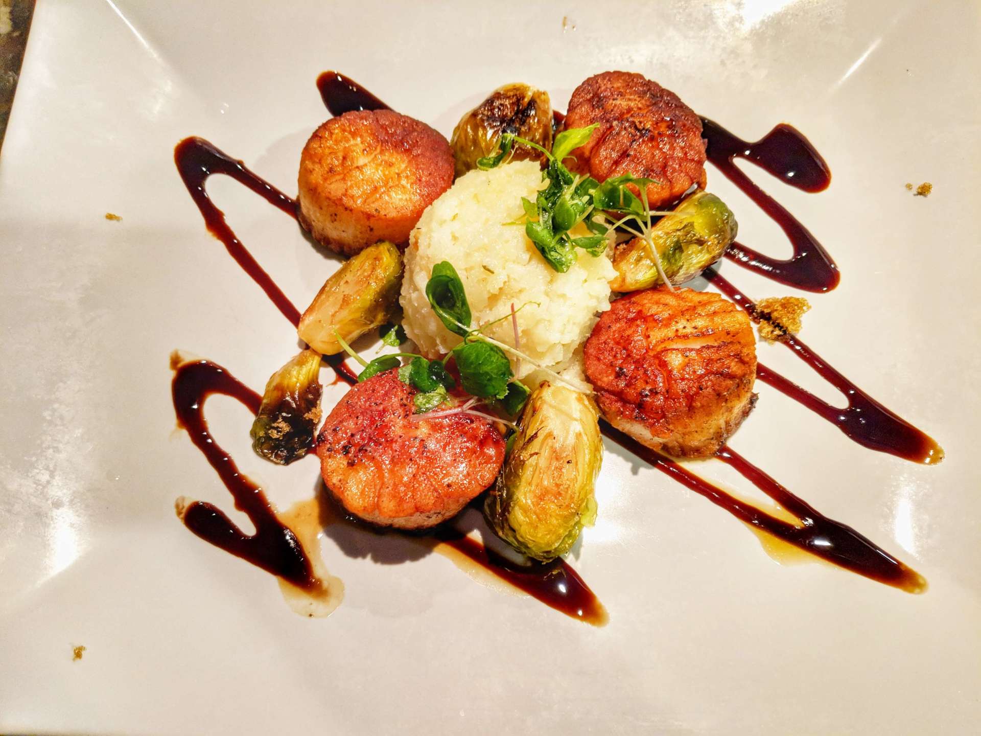 A white plate topped with scallops mashed potatoes and sauce
