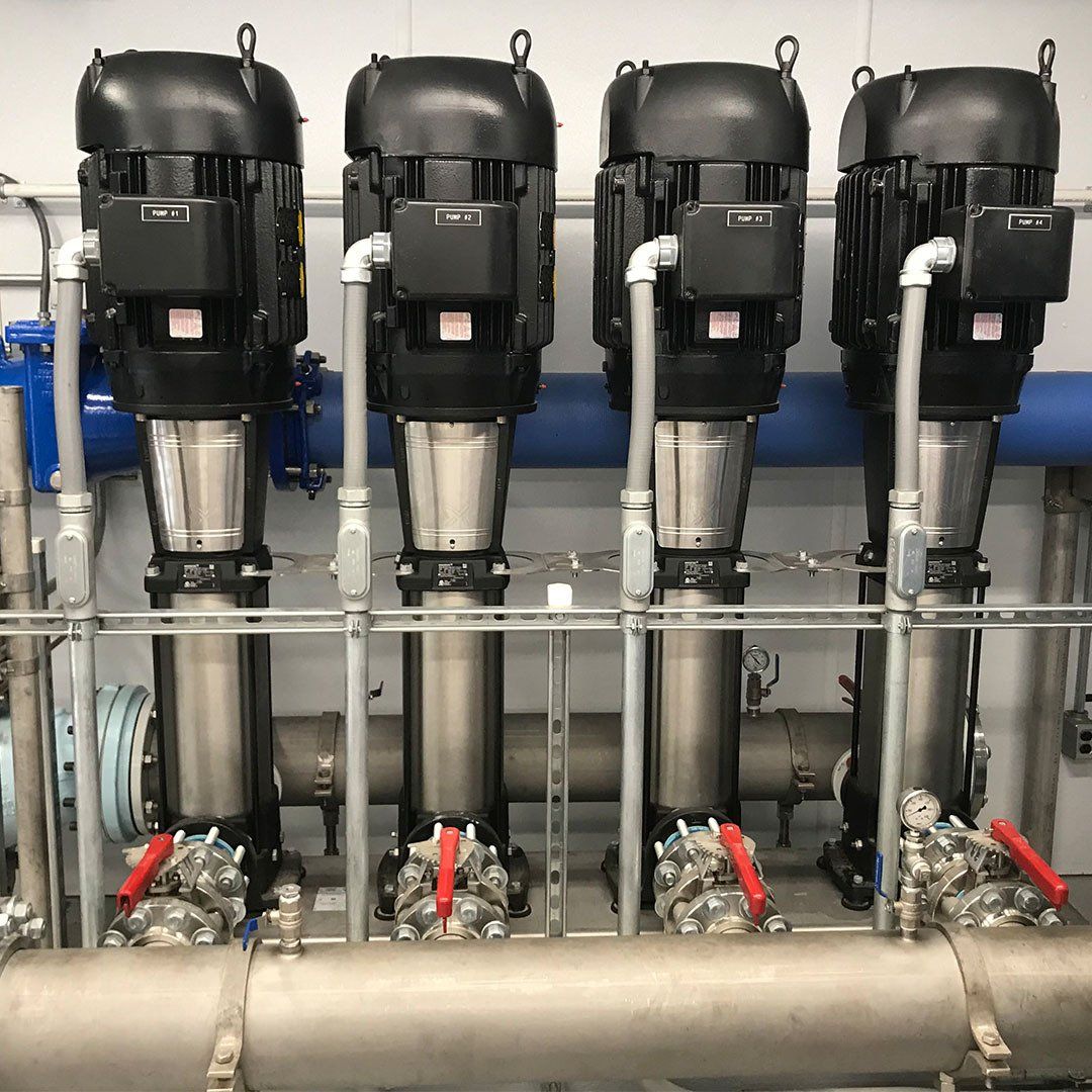A row of stainless steel pumps and pipes in a room