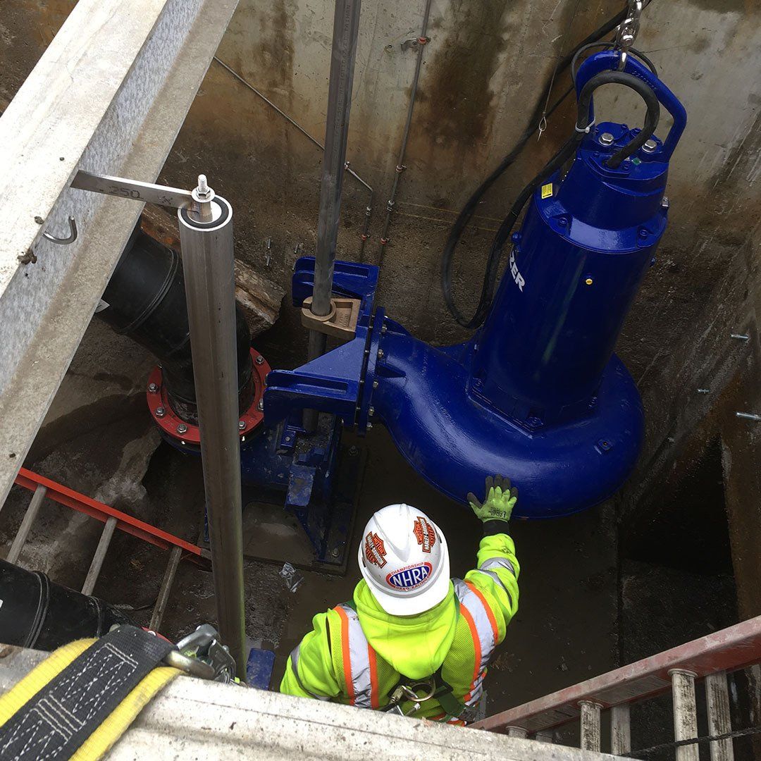 A man wearing a hard hat and safety vest is working on a blue pump