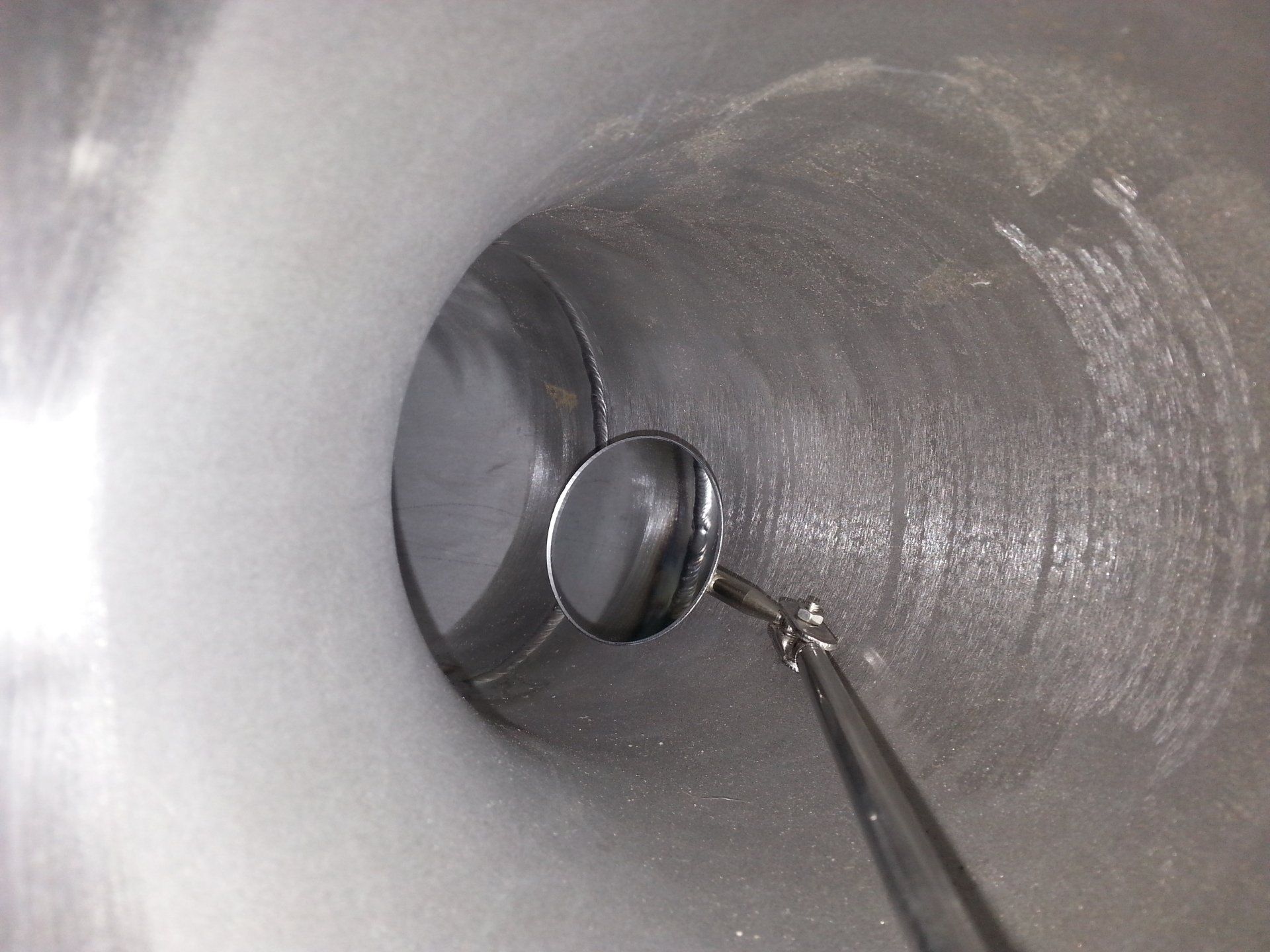 In een metalen buis reflecteert een inspectiespiegel de andere kant.