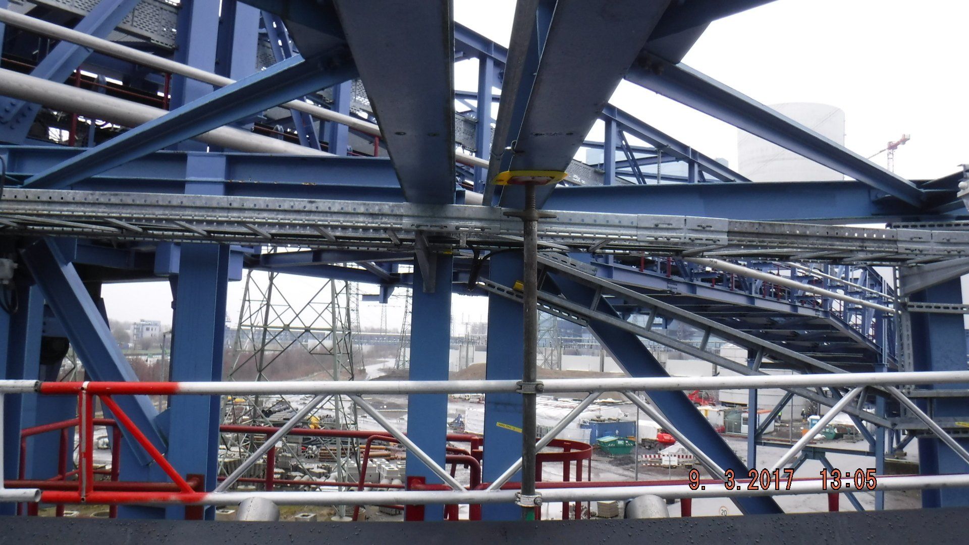 Blauwe industriële constructie met metalen balken, loopbruggen en bekabeling; zicht vanaf een reling.