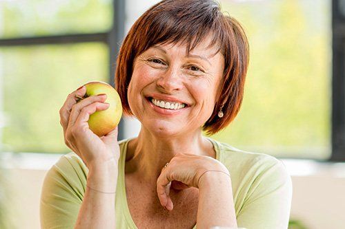 Dental Implants Older woman smiling while holding an apple