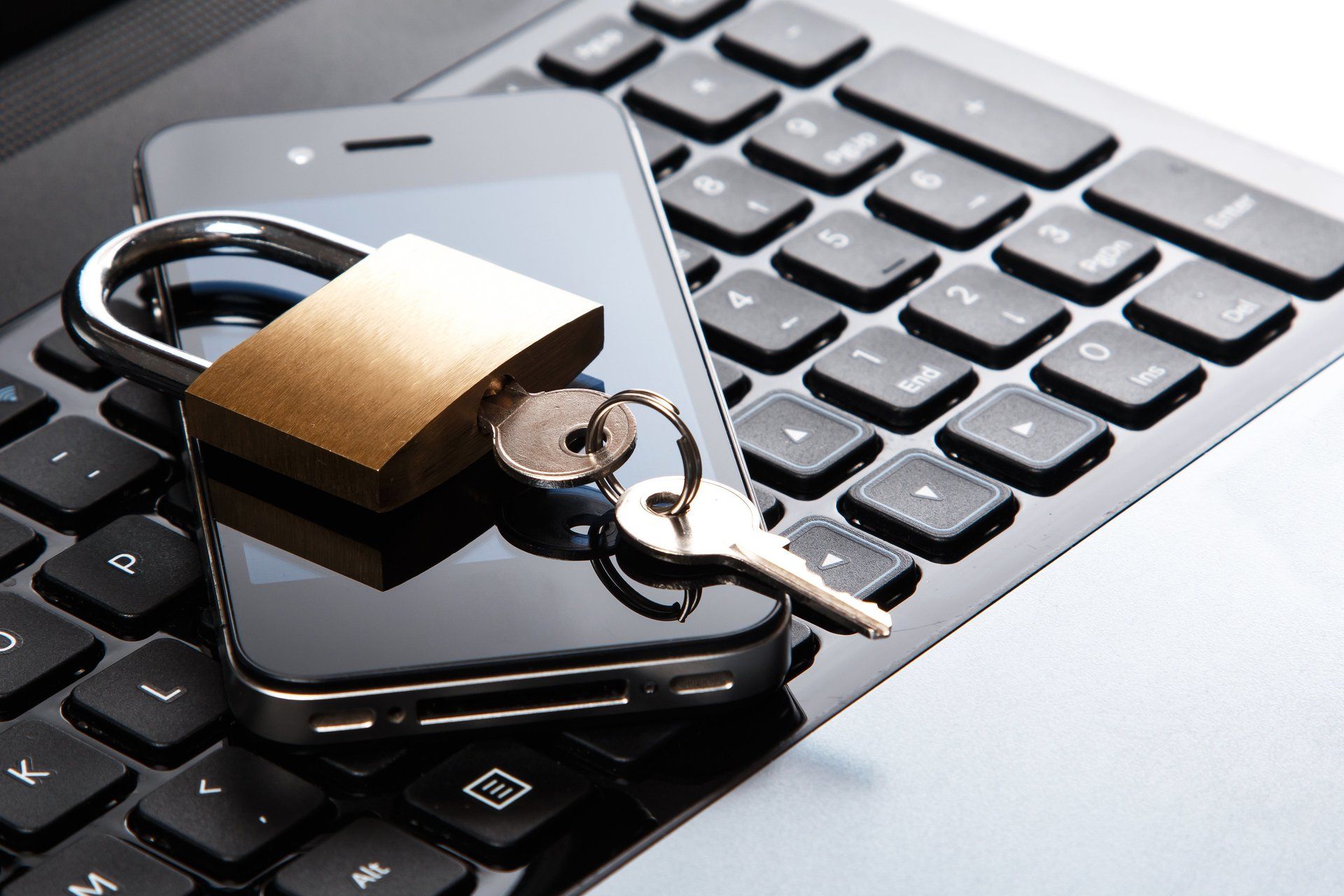 A cell phone with a padlock and keys on top of a laptop keyboard