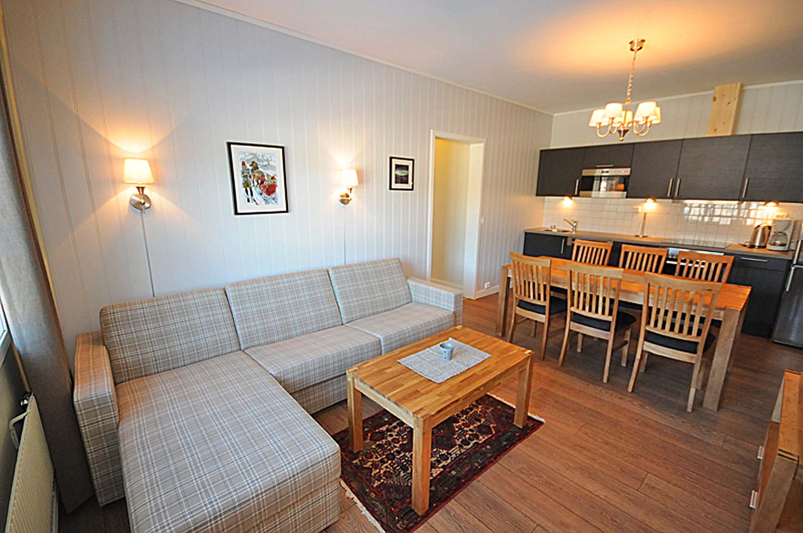 En stue med sofa , bord , stoler og kjøkken.