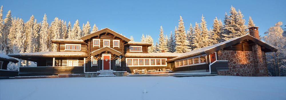 En stor tømmerhytte midt i en snødekt skog.